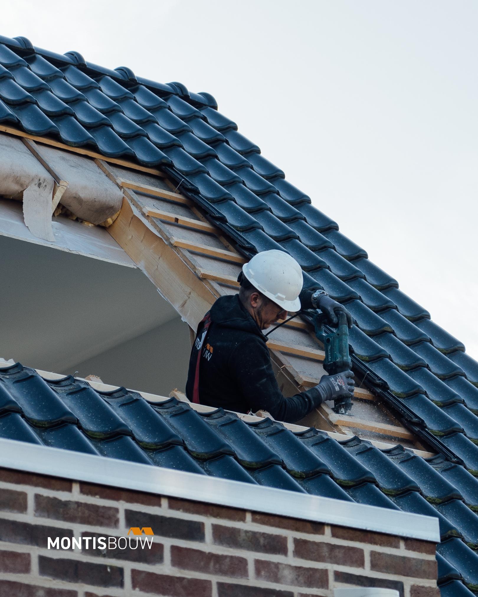 Werker bevestigt dakkapel op dak met blauwe pannen en veiligheidshelm