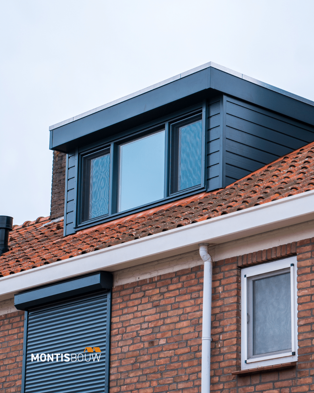 Donkerblauwe dakkapel met drie grote ramen op bakstenen woning