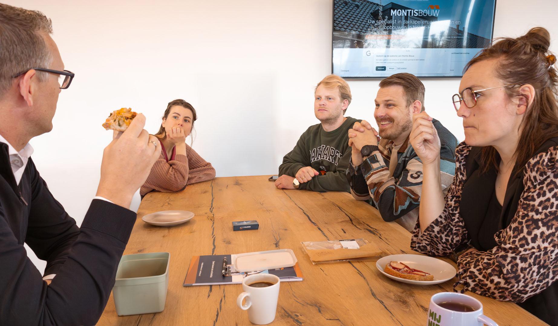 Medewerkers zitten informeel rond tafel met koffie en eten