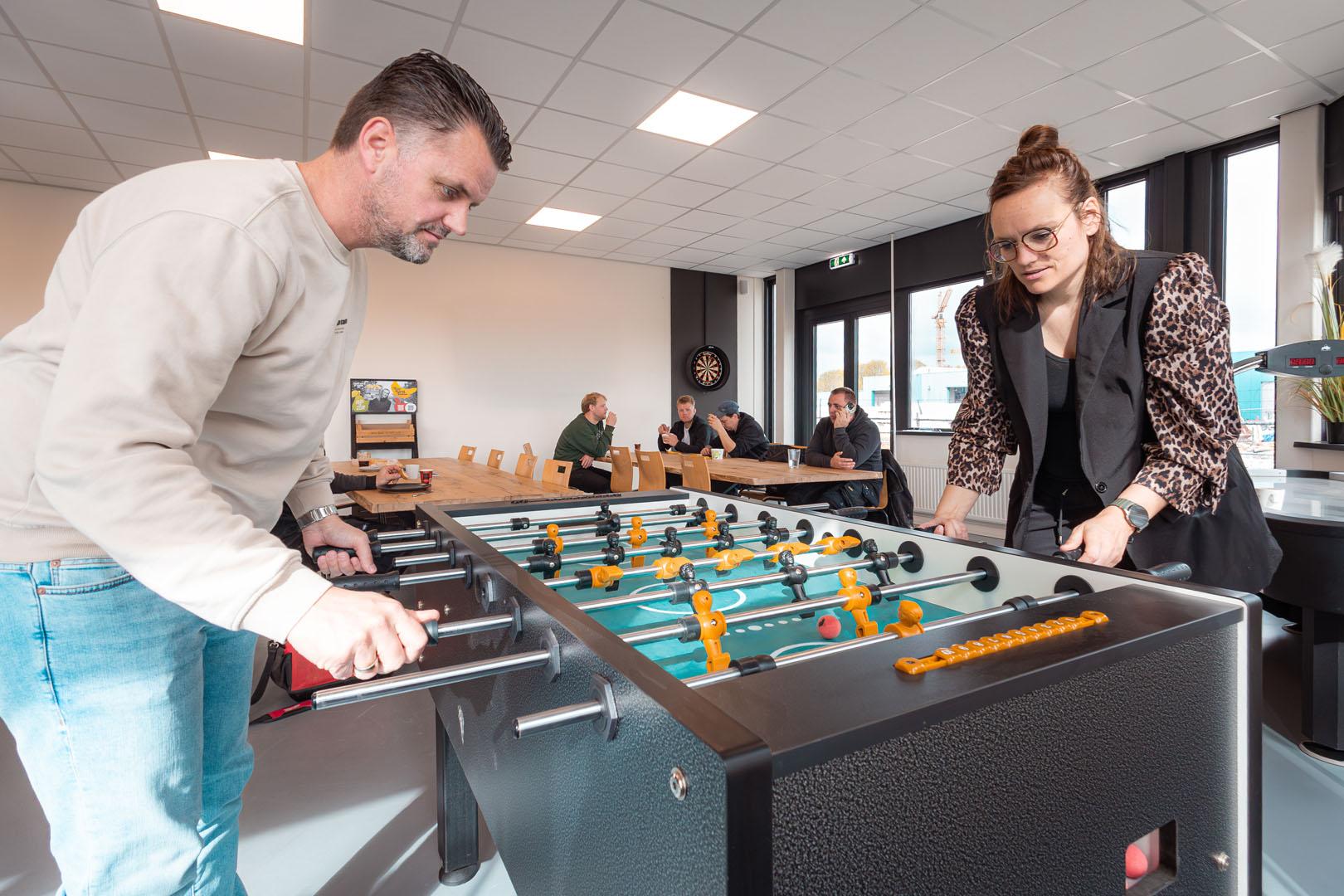 Medewerkers spelen tafelvoetbal in kantoor, anderen kijken toe