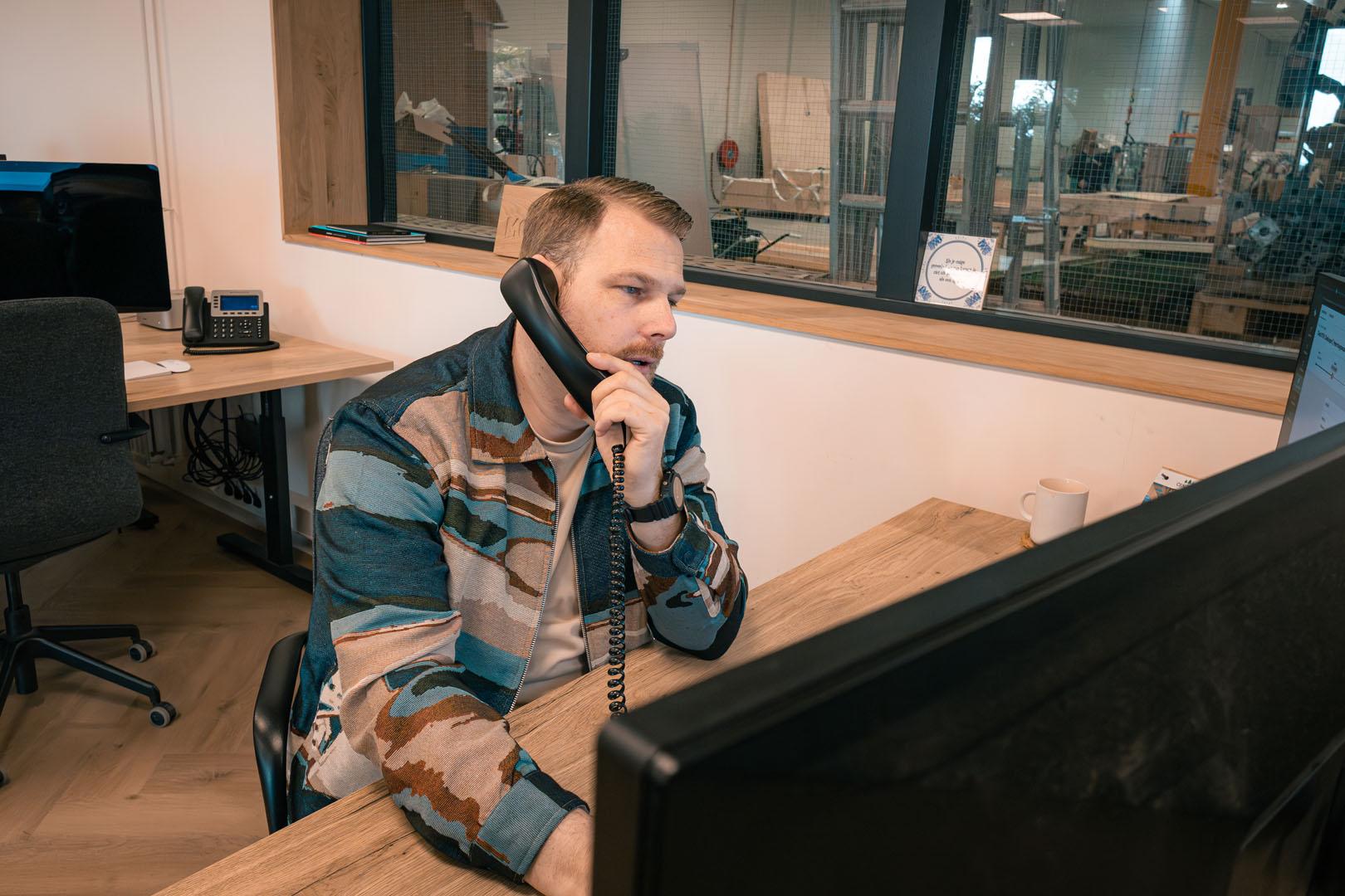Man telefooneert op kantoor met bouwmaterialen op achtergrond