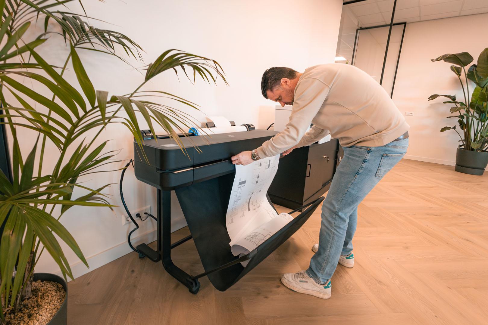 Man haalt bouwplannen uit printer in moderne kantooromgeving