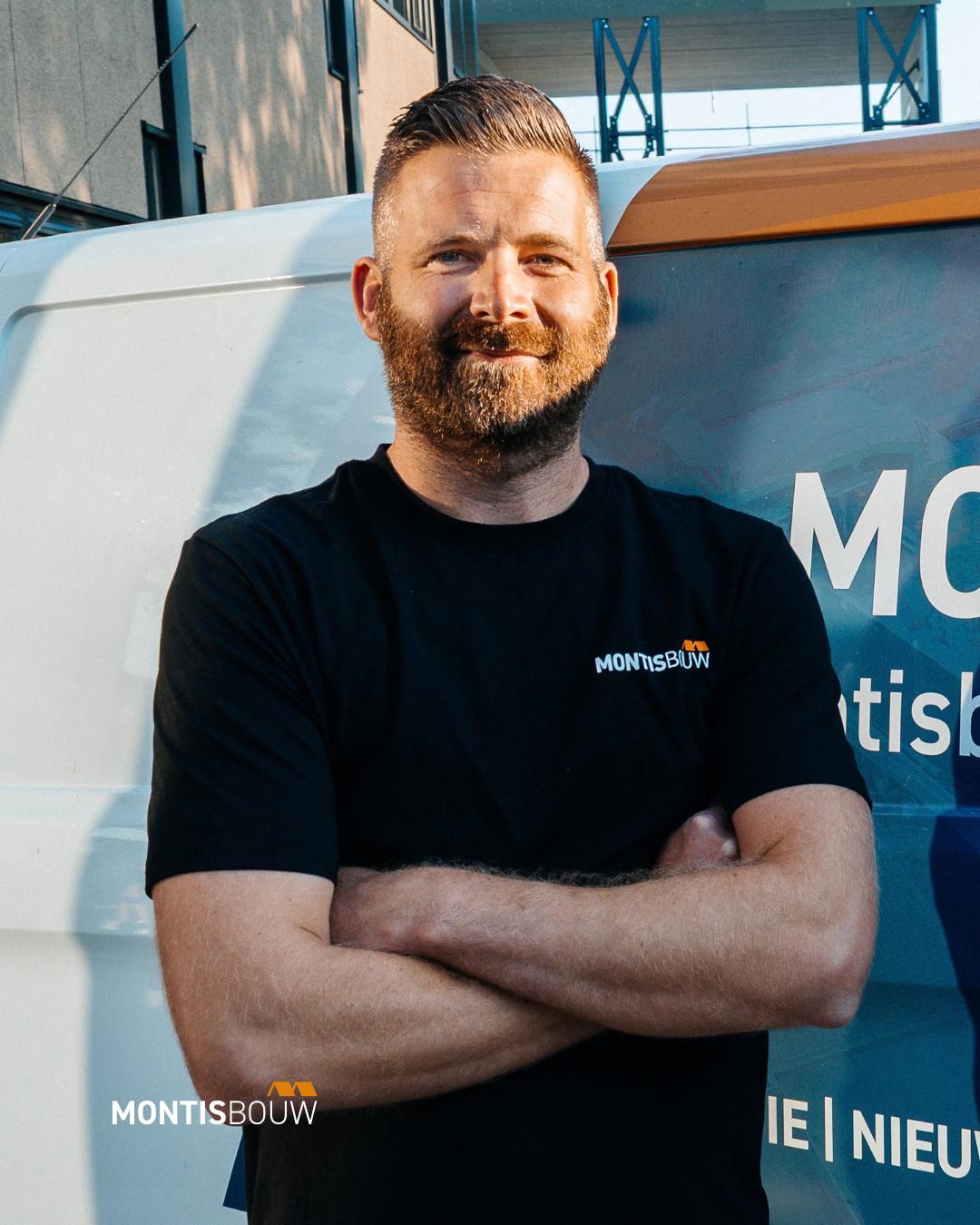 Man in zwart Montis Bouw shirt met gekruiste armen voor bouwplaats