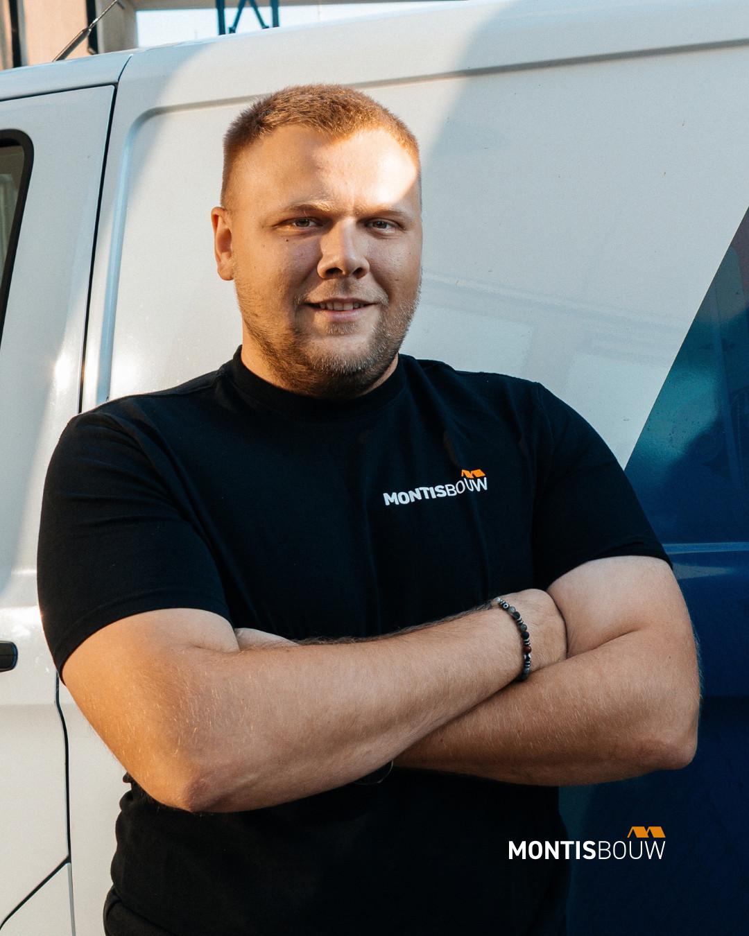 Man in Montisbouw-shirt met gekruiste armen voor bestelwagen