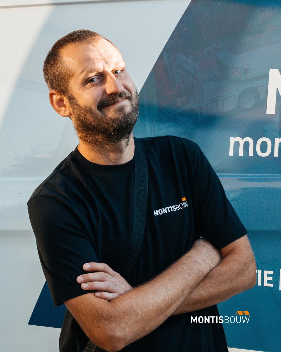 Man in Montisbouw-shirt met gekruiste armen voor bedrijfsachtergrond