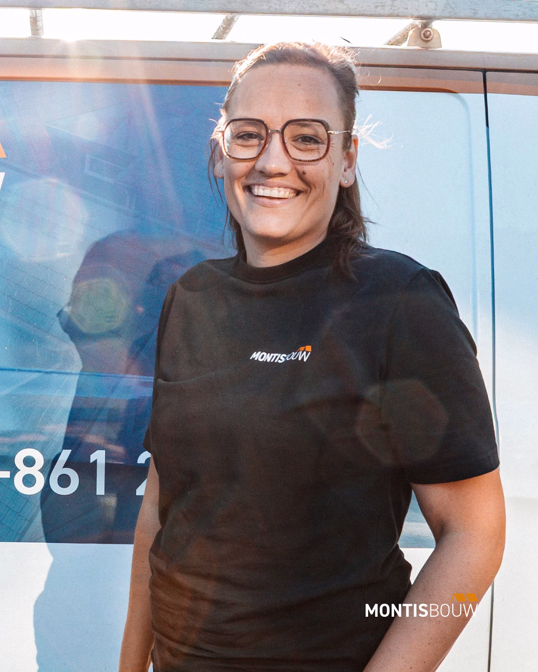 Persoon met bril in zwart MONTIS-shirt, lachend voor blauwe achtergrond