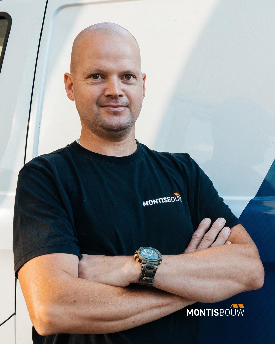 Man in zwart Montisbouw-shirt met gekruiste armen voor bestelwagen