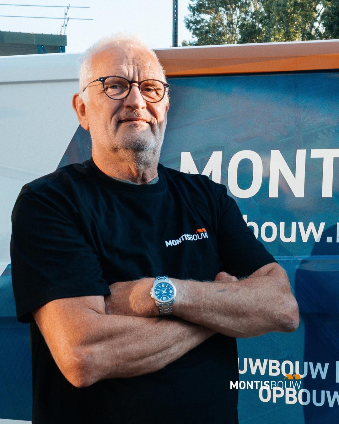 Man met gekruiste armen voor MONTISBOUW voertuig op bouwterrein